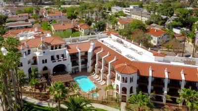 Aerial view of the Santa Barbara Inn, showcasing a pool and palm trees amid lush greenery on a sunny day