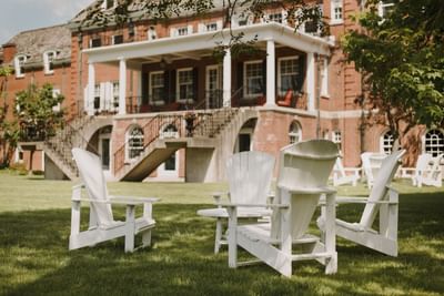 Adirondack chairs arranged on the lawn outside the historic brick facade at Spencer Hotel & Conference Centre