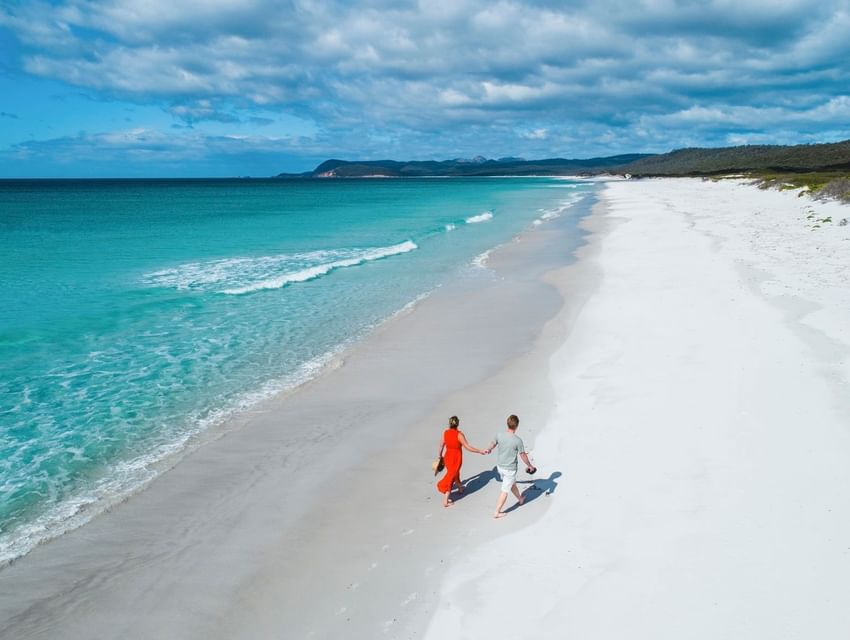 Distant view of a couple strolling by the beach on a sunny day near Freycinet Lodge
