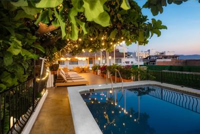 Evening view of the rooftop swimming pool with lounge chairs and glowing string lights at Casa Dona Susana