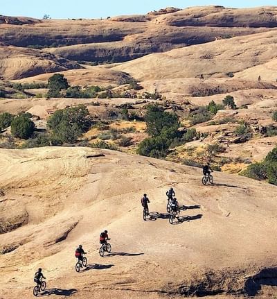 Mountain bikers navigate the rocky Slickrock Trail, surrounded by rugged desert landscapes near Moab Valley Inn