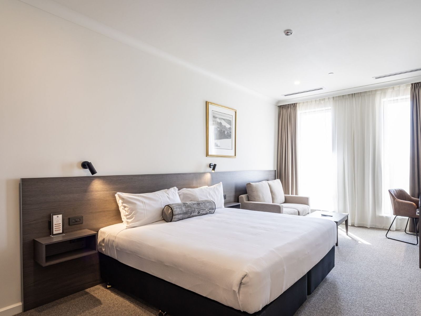 Deluxe King room featuring a king-size bed, armchair, and large windows with sheer curtains at Duxton Hotel Perth