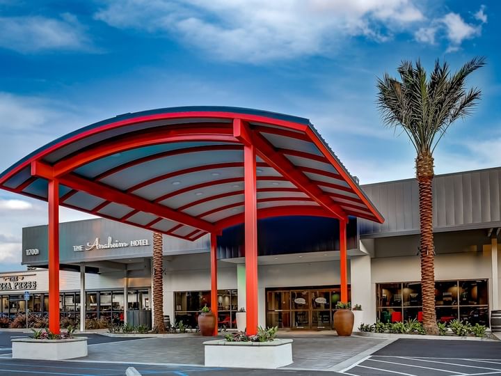 The exterior of the hotel with a red canopy and palm trees