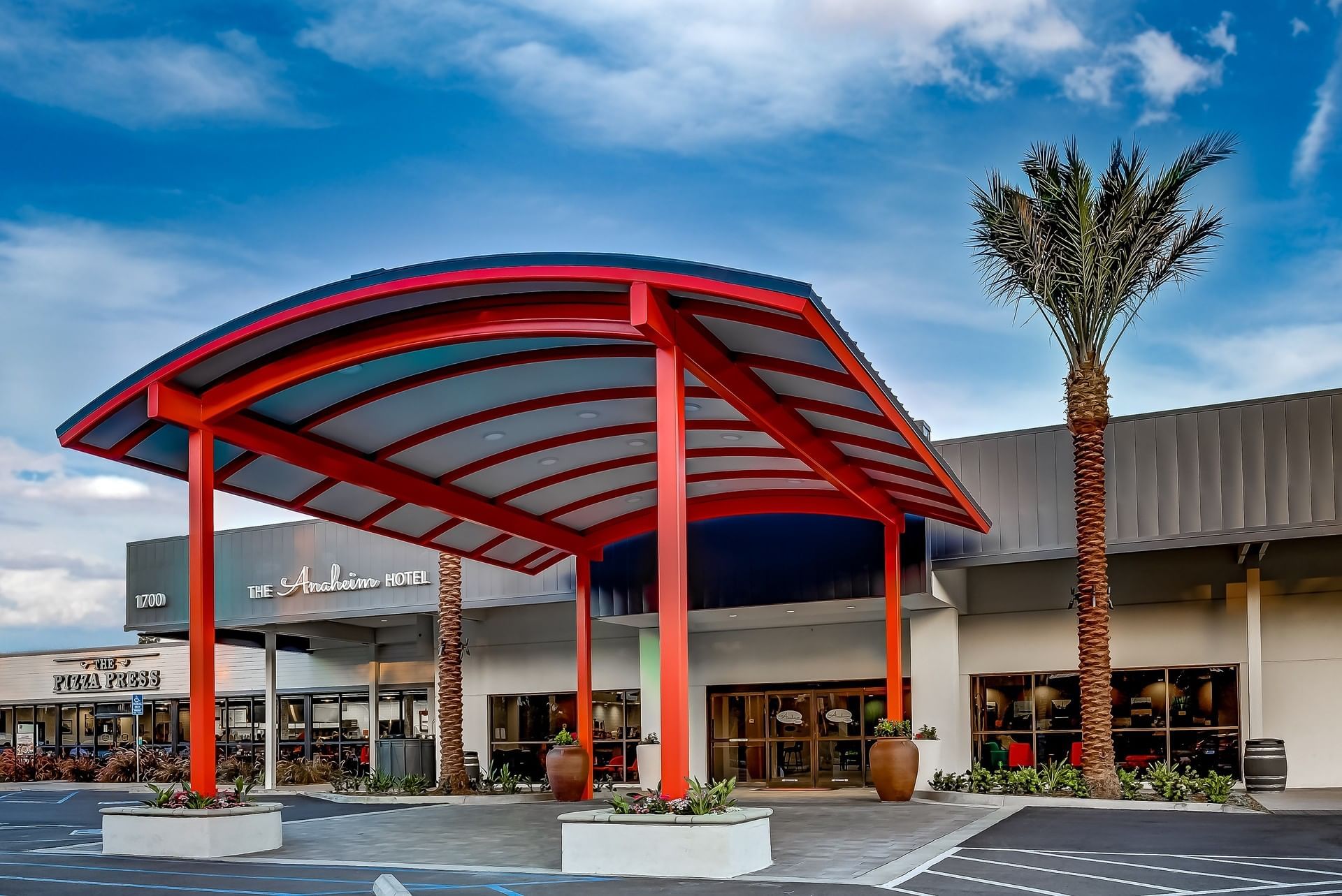 The exterior of the hotel with a red canopy and palm trees