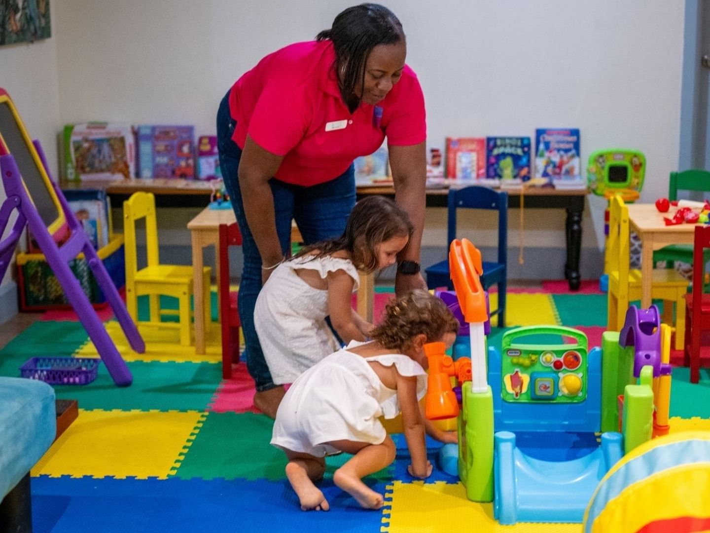 A caregiver and two young children playing with toys in a playroom at Savannah Beach Hotel.