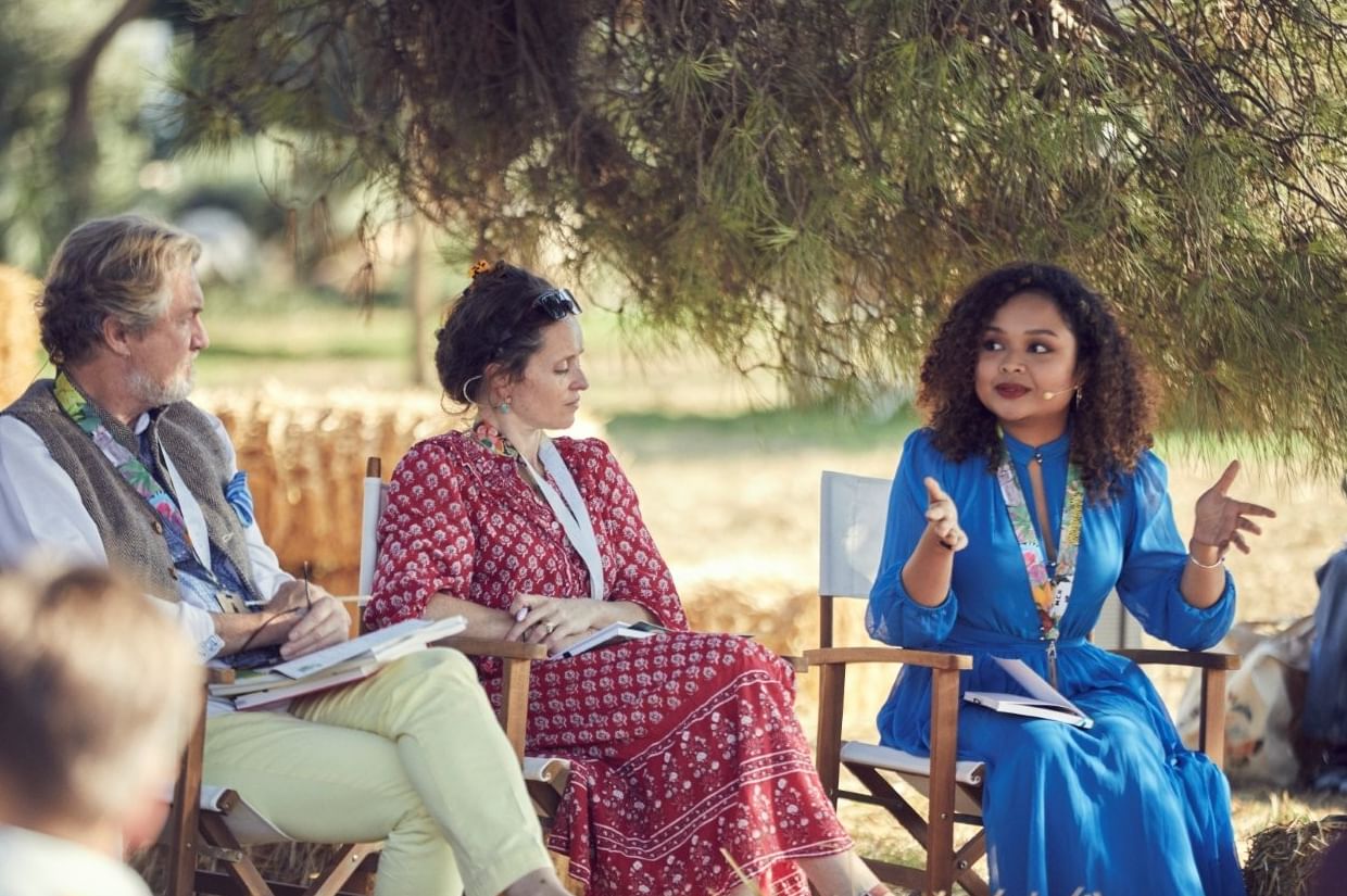 Outdoor panel with a woman in a blue dress speaking to two guests seated on director’s chairs near Marbella Club