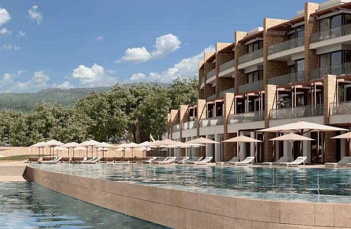 Piscina di lusso con ombrelloni e lettini, affianco a un hotel moderno.