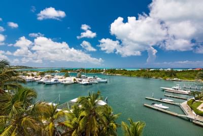 Aerial view of white luxury yachts and catamarans docked in turquoise Turtle Cove waters under a blue sky at Zenza Hotel