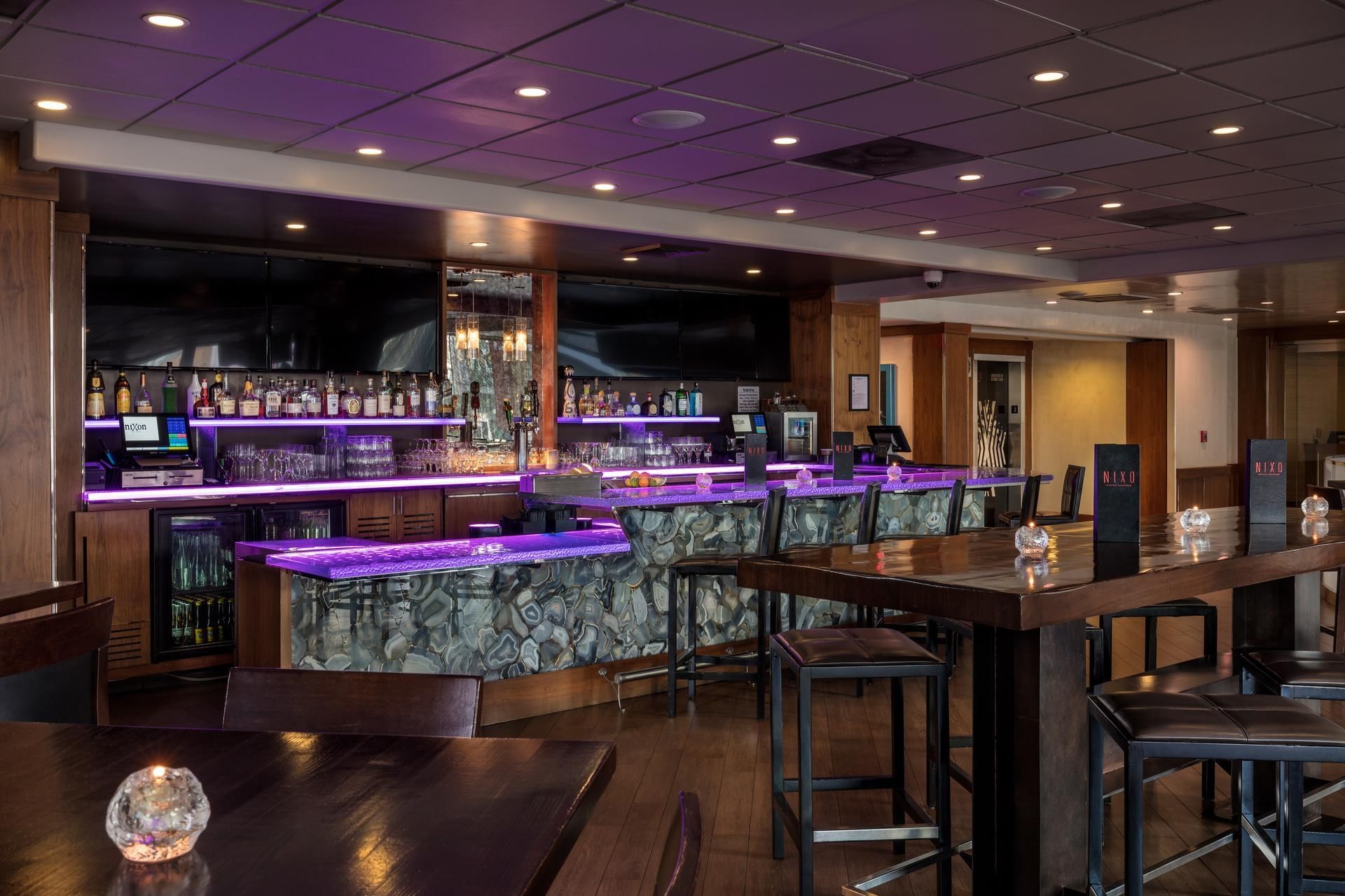 A dimly lit bar with purple lighting, a bar counter, and several tables and stools.