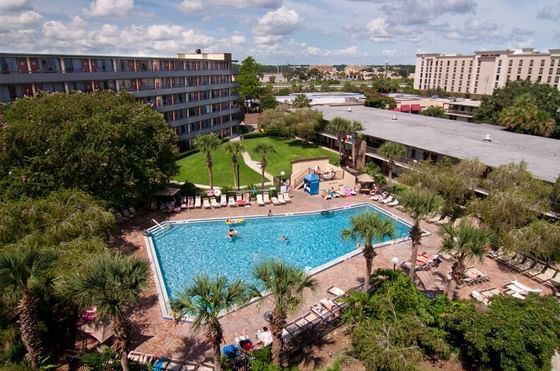 Aerial view of an expansive outdoor swimming pool encircled by palm trees and guest buildings at Rosen Inn International