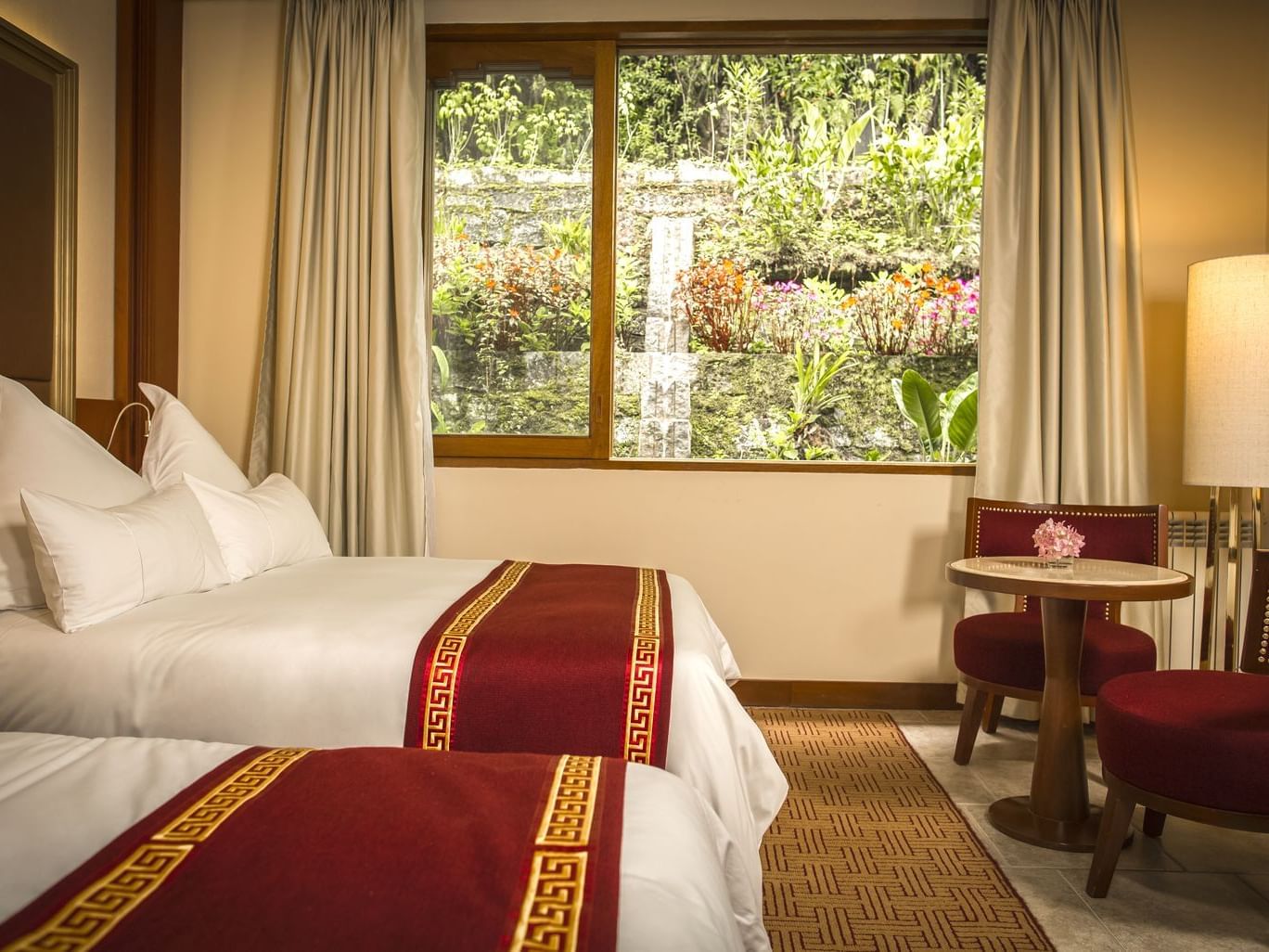 Sumaq Deluxe with Garden View featuring two beds with burgundy runners and a window overlooking lush gardens at Sumaq Machu Picchu Hotel