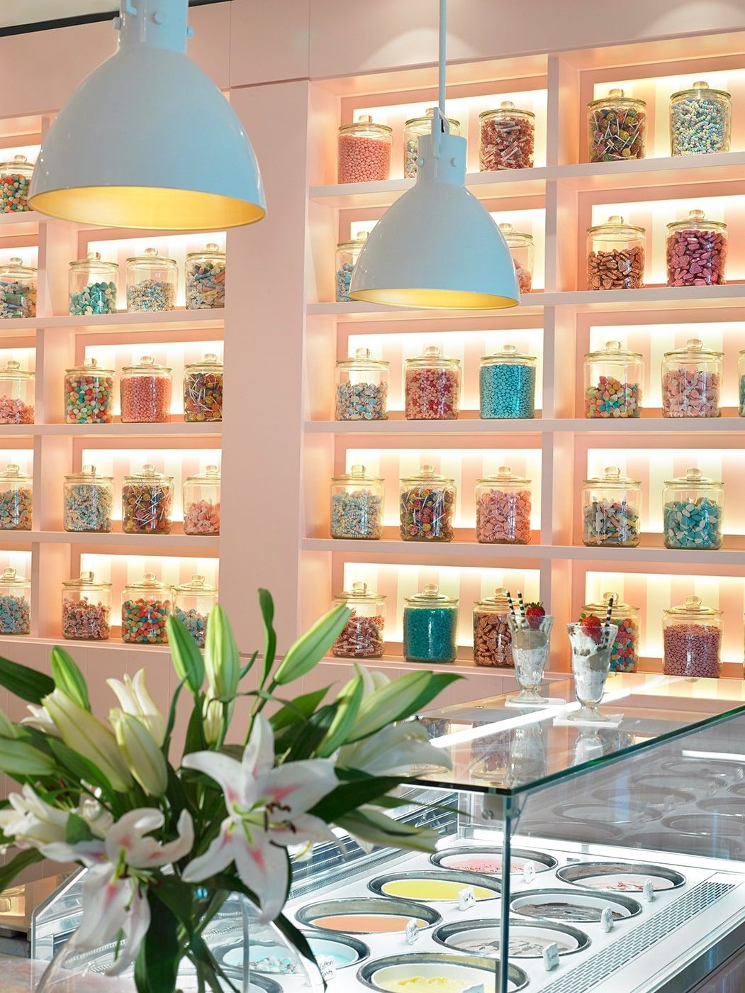 A colorful ice cream shop with a glass case, shelves of candy, and flowers.