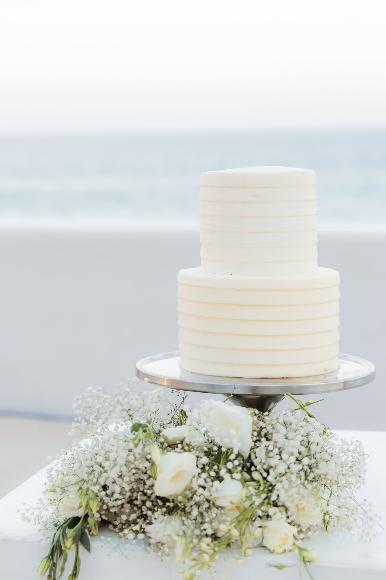 Two-tier white wedding cake with floral decor at Marquis Los Cabos Resort