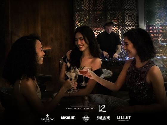 Three women toasting with cocktails as a DJ plays in the background in 2 Lam Son at Park Hyatt Saigon