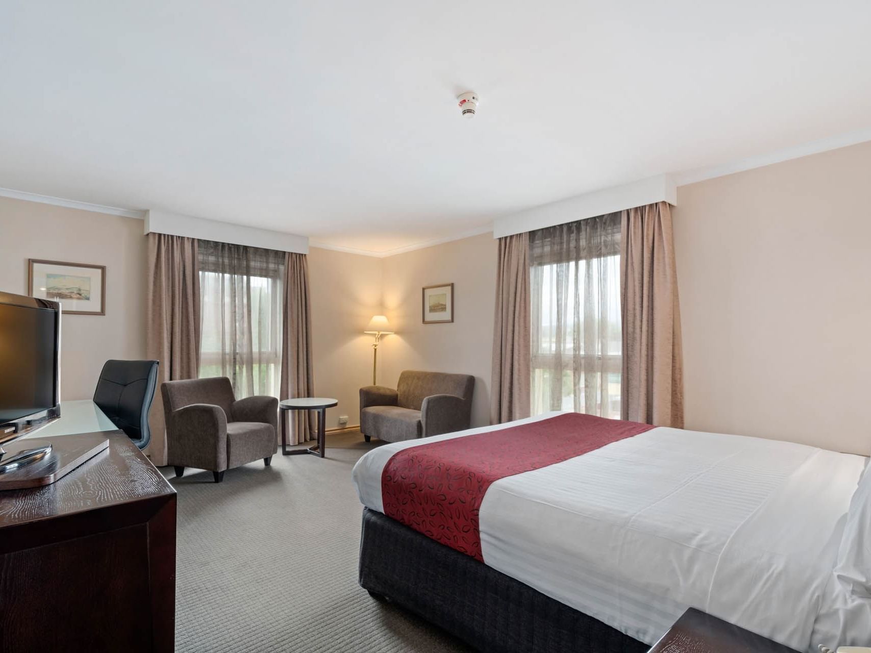 Large bed arranged by working area and sofa in Deluxe King Room at Hotel Grand Chancellor Launceston