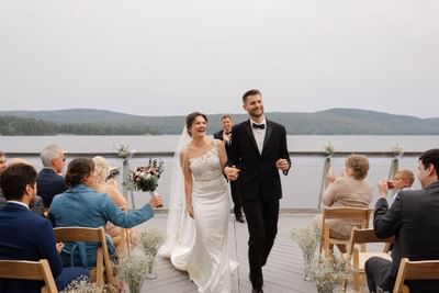 Bride and groom walking down with seated guests on the side in The Lodge at Schroon Lake