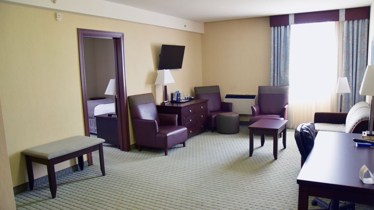 Hotel room with bed, desk, chairs, TV, and window with curtains.