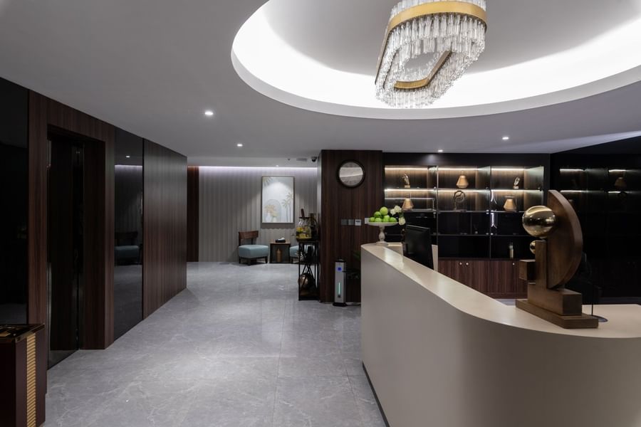 Curved reception desk by wood-paneled walls under an oval crystal chandelier in a lobby at Warwick Al Taif Hotel