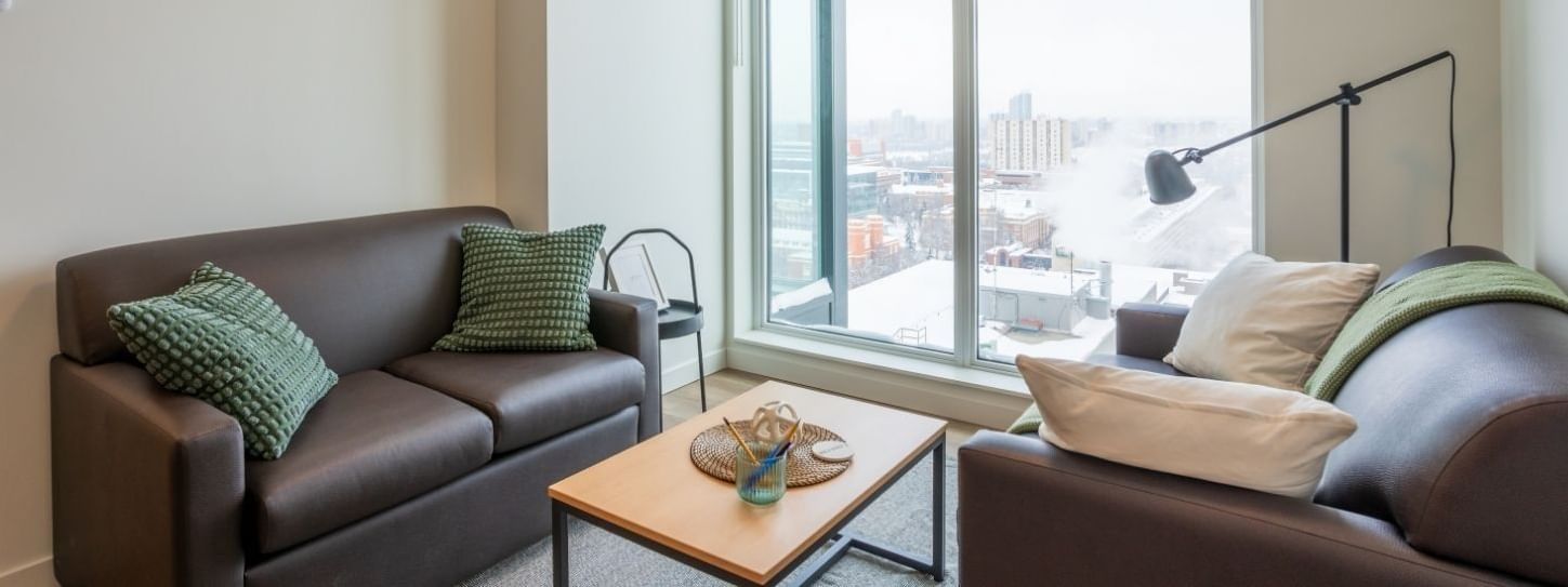 A cozy and well decorated sitting area with floor to ceiling views onto a snowy cityscape below.