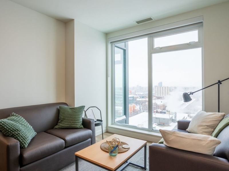 A cozy and well decorated sitting area with floor to ceiling views onto a snowy cityscape below.