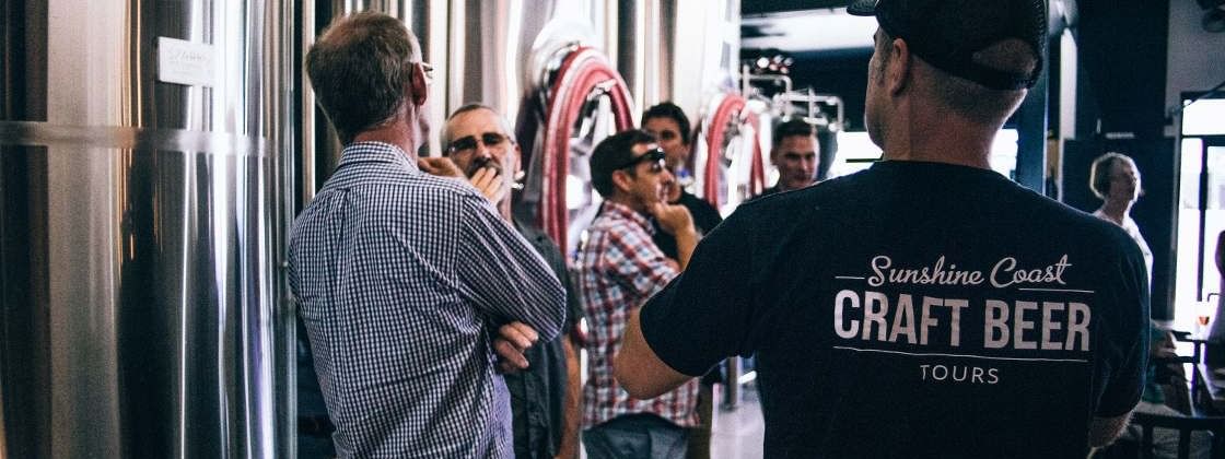 Group of people engaging in a brewery tour, surrounded by large fermentation tanks near Novotel Sunshine Coast Resort
