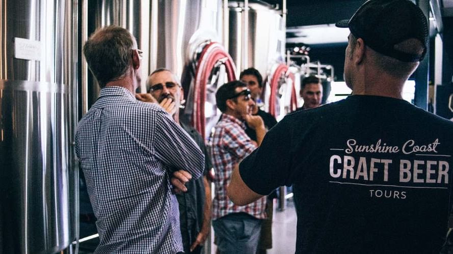 Group of people engaging in a brewery tour, surrounded by large fermentation tanks near Novotel Sunshine Coast Resort