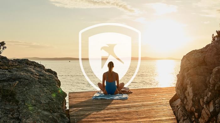 Woman meditating on a dock with a digital security shield icon overlaid at Falkensteiner Hotels & Residences