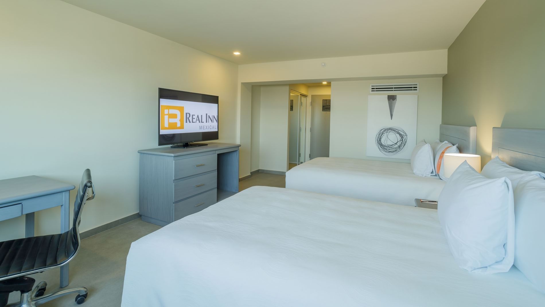 2 Double Deluxe room including a flat-screen TV, a desk area, and white textured bedding at Real Inn Mexicali