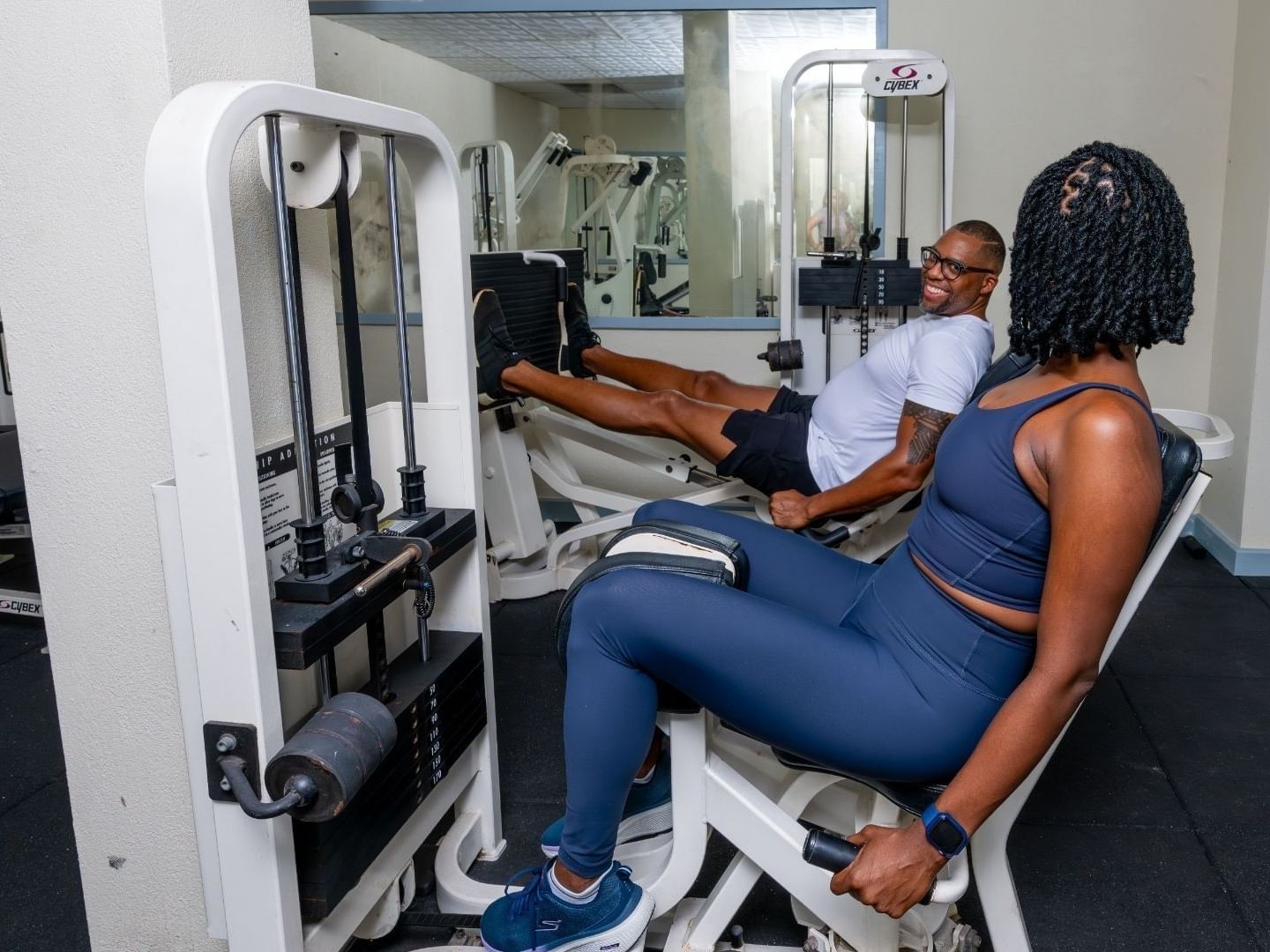 Woman and man using leg press machine in gym at Savannah Beach Hotel.