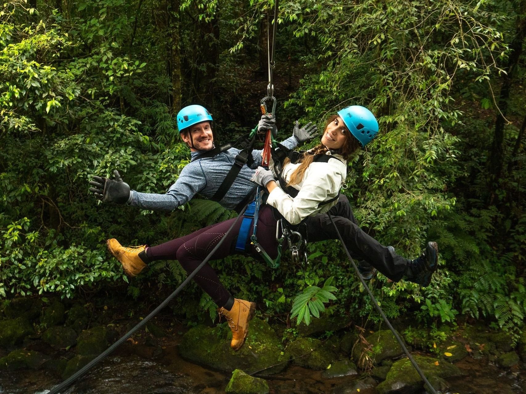 Two people ziplining over a lush forest near El Silencio Lodge and Spa