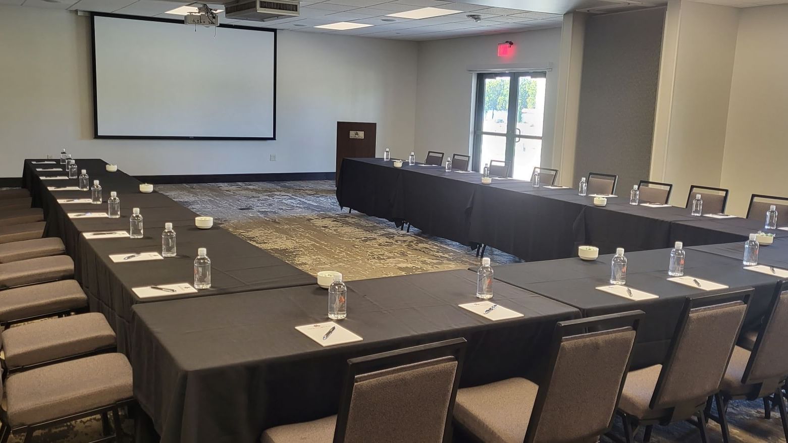 Modern conference table set with water glasses, pens, & a projector screen in Boardroom at Shangri-La Monkey Island
