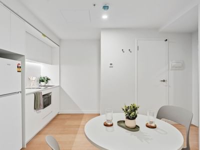 Modern white kitchen with appliances, dining area, and potted plant at UniLodge Brisbane City.