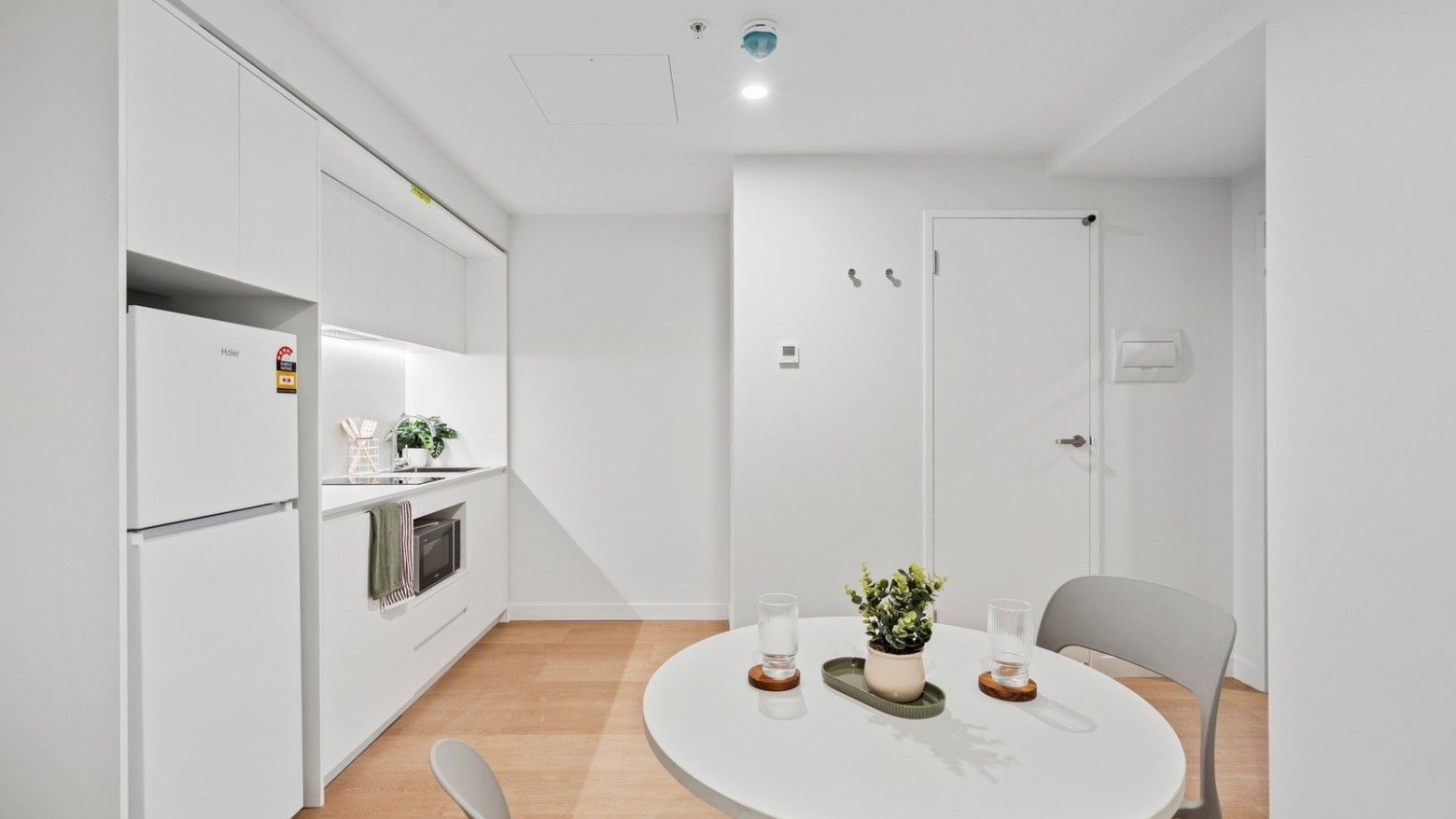 Modern white kitchen with appliances, dining area, and potted plant at UniLodge Brisbane City.