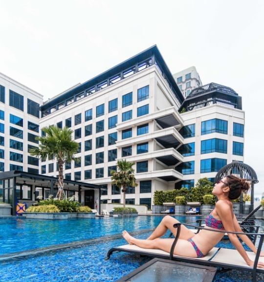 Woman in bikini relaxing on lounge chair by swimming pool at Park Hotel Group