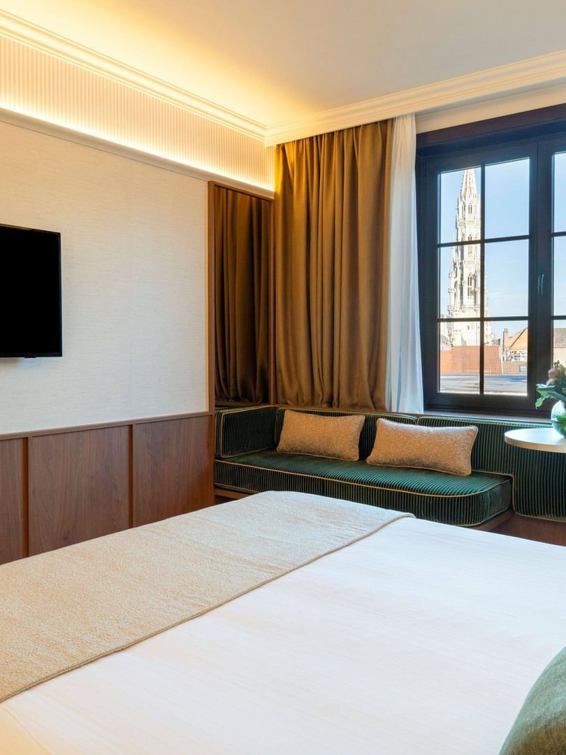 Moderne hotelkamer met tweepersoonsbed, flatscreen-tv, zithoek bij raam en uitzicht op historische toren