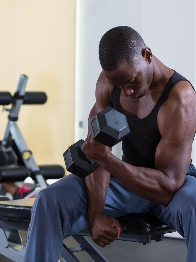 Man lifting a weight by a gym bench under bright light surrounding fitness gear at Warwick Paradise Island Bahamas