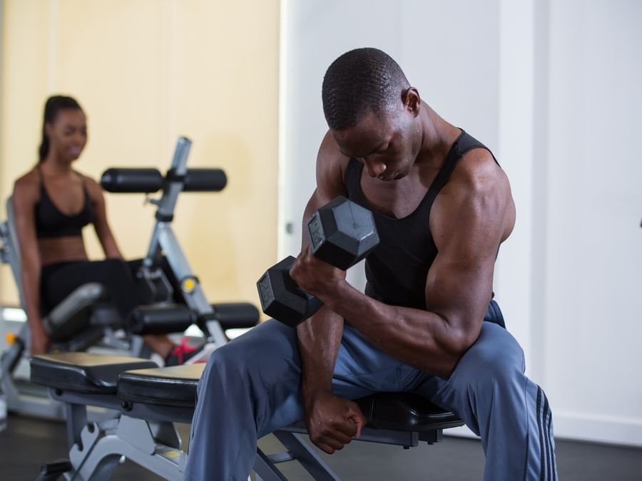 Man lifting a weight by a gym bench under bright light surrounding fitness gear at Warwick Paradise Island Bahamas