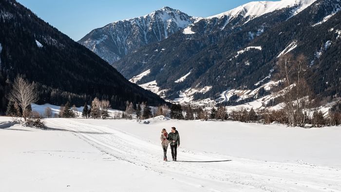 Couple walking through a snow path with mountain backdrop at Falkensteiner Hotel Antholz