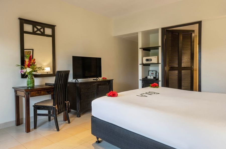 Dark wood desk by a bed under a wall mirror near a recessed safe in Suite at The Naviti Resort - Fiji
