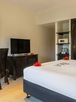 Dark wood desk by a bed under a wall mirror near a recessed safe in Suite at The Naviti Resort - Fiji