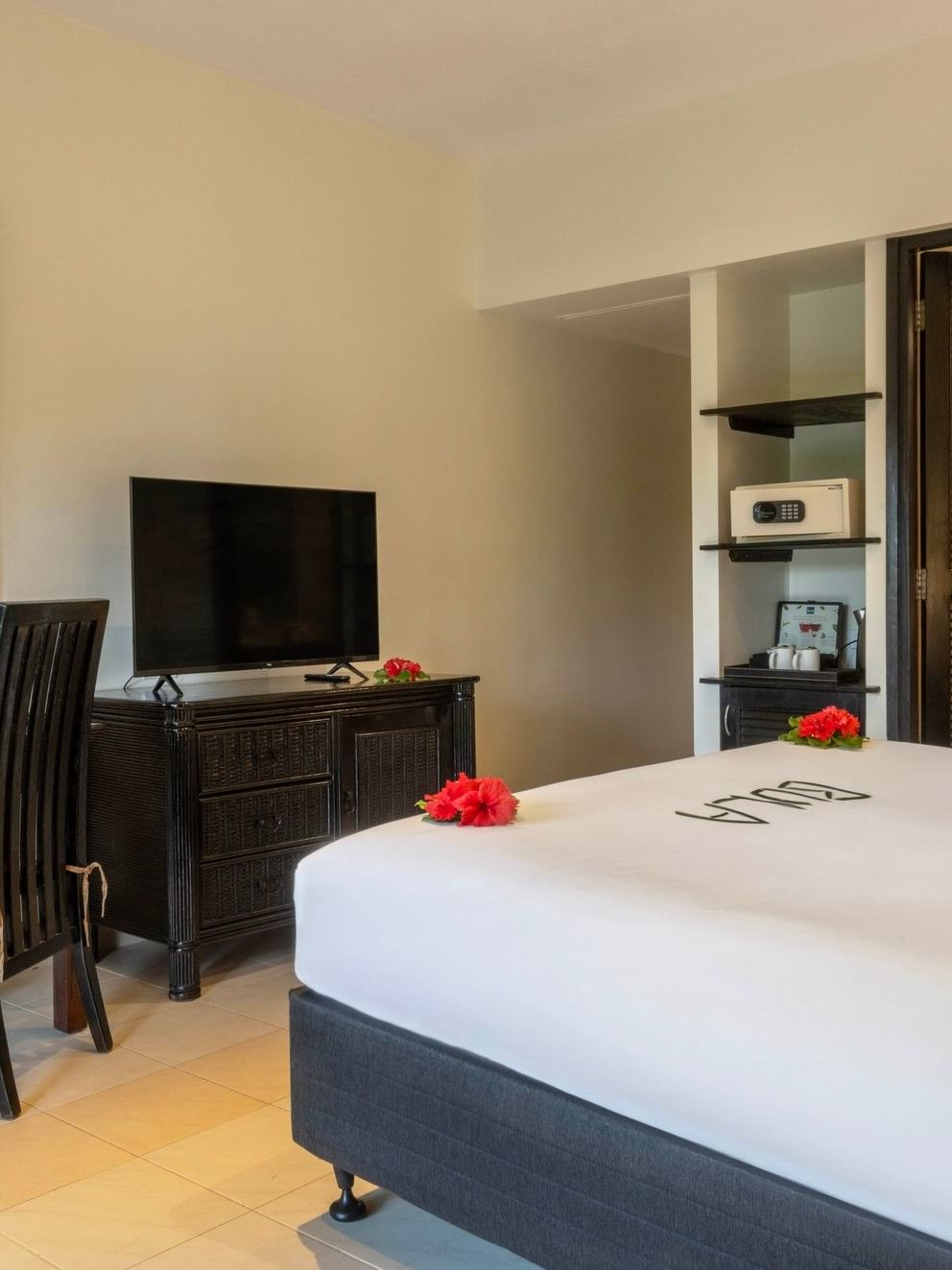 Dark wood desk by a bed under a wall mirror near a recessed safe in Suite at The Naviti Resort - Fiji