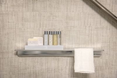 Silver bathroom shelf at The Riverwalk Plaza Hotel with four PURE brand toiletries and a white towel against a beige wall