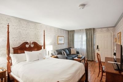 Four-poster bed facing TV screen beside a sofa and coffee table in the guest room at Avon Old Farms Hotel