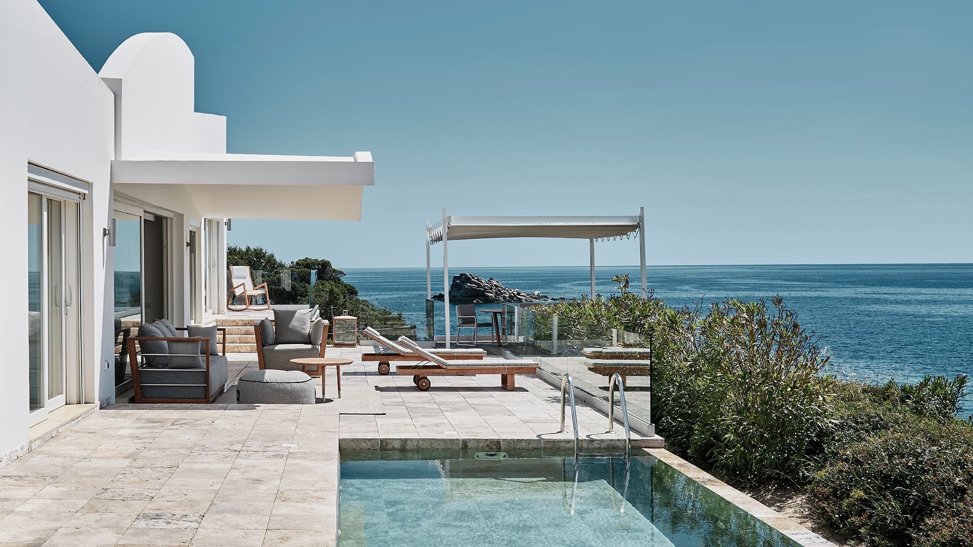 Modern villa with a pool, lounge chairs, and seating area overlooking the sea at Falkensteiner Resort Capo Boi