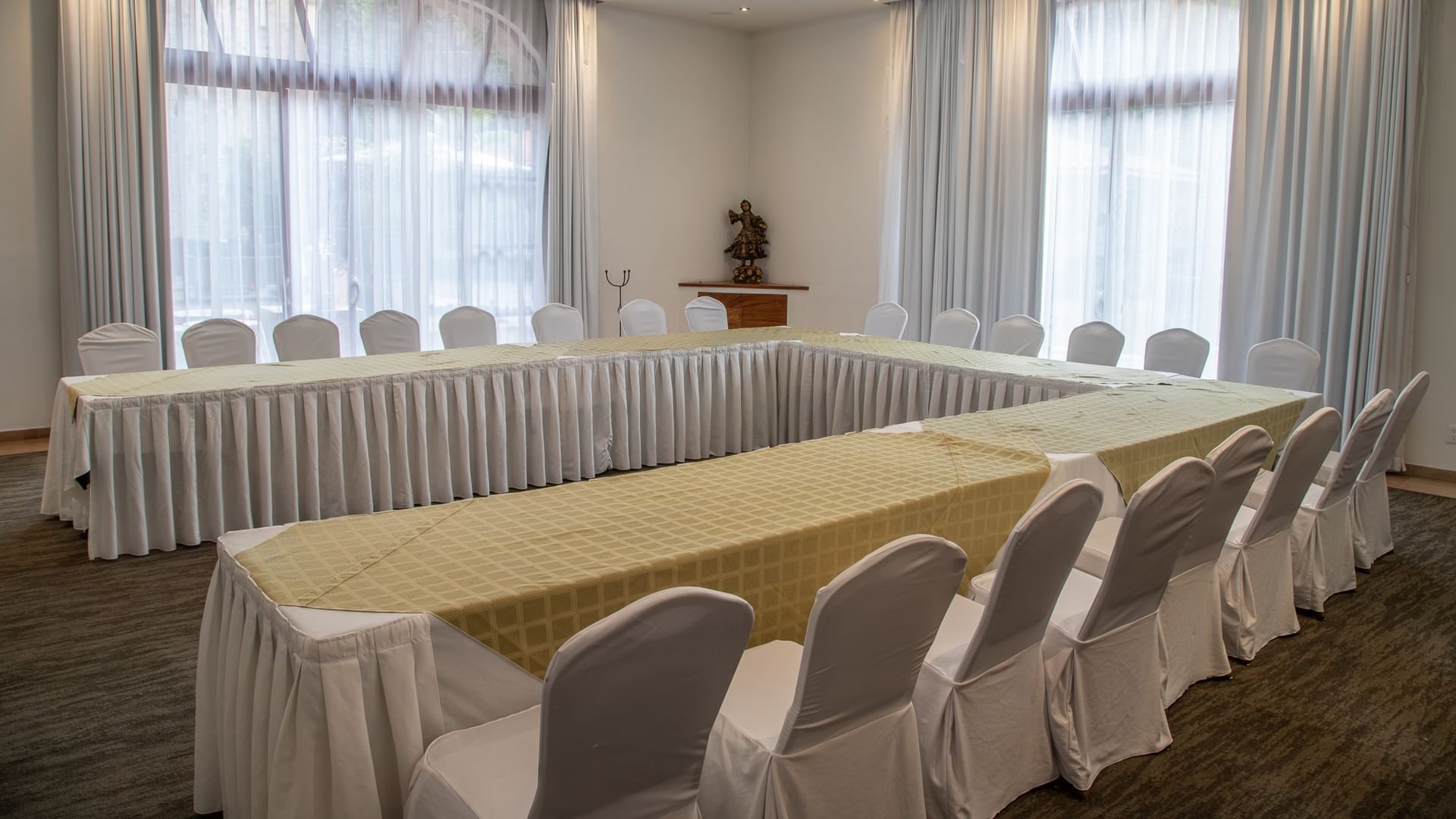 Salón de eventos con mesas en forma de U, sillas blancas y cortinas elegantes en Quinta Real Guadalajara