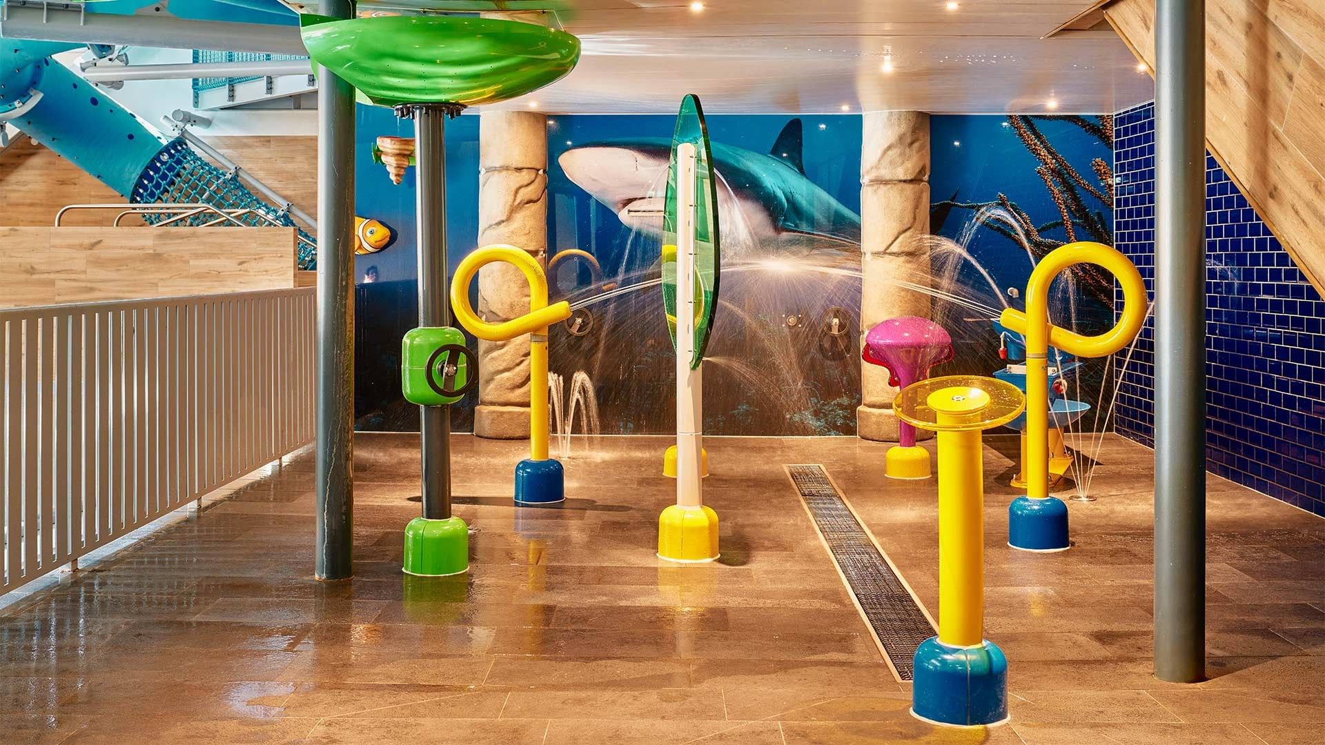 Colorful water play area with shark mural on the wall and various interactive water features.