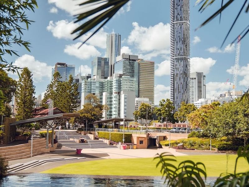 Roma Parkland features a modern urban park with green lawns, trees, and a city skyline with tall buildings in the background.