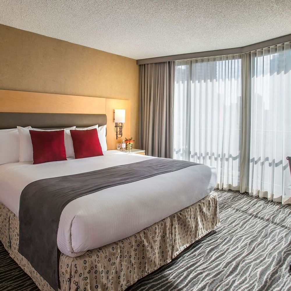 King bed with red pillows by large windows under soft light in Accessible Deluxe Rooms at Warwick Seattle