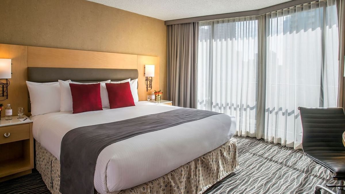 King bed with red pillows by large windows under soft light in Accessible Deluxe Rooms at Warwick Seattle