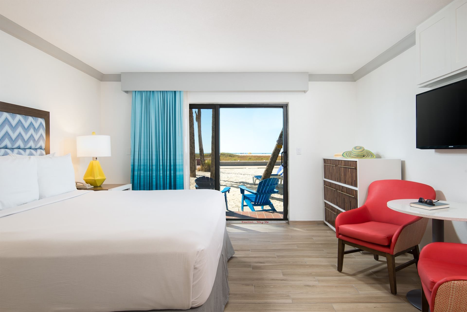 A wide view of a hotel room with a bed, chair, table, TV, and door leading to a balcony.